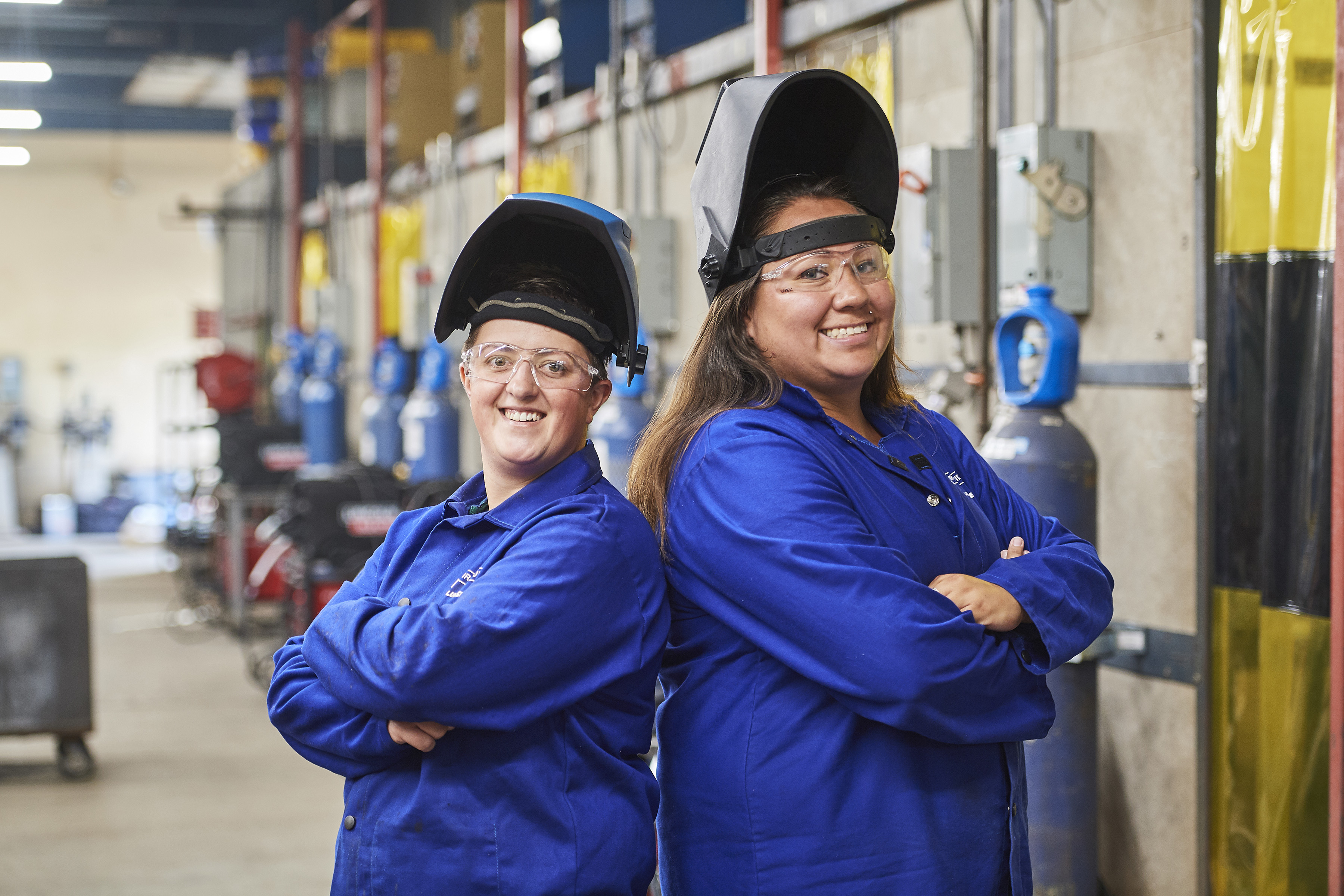 Two welding students standing back to back in welding bay